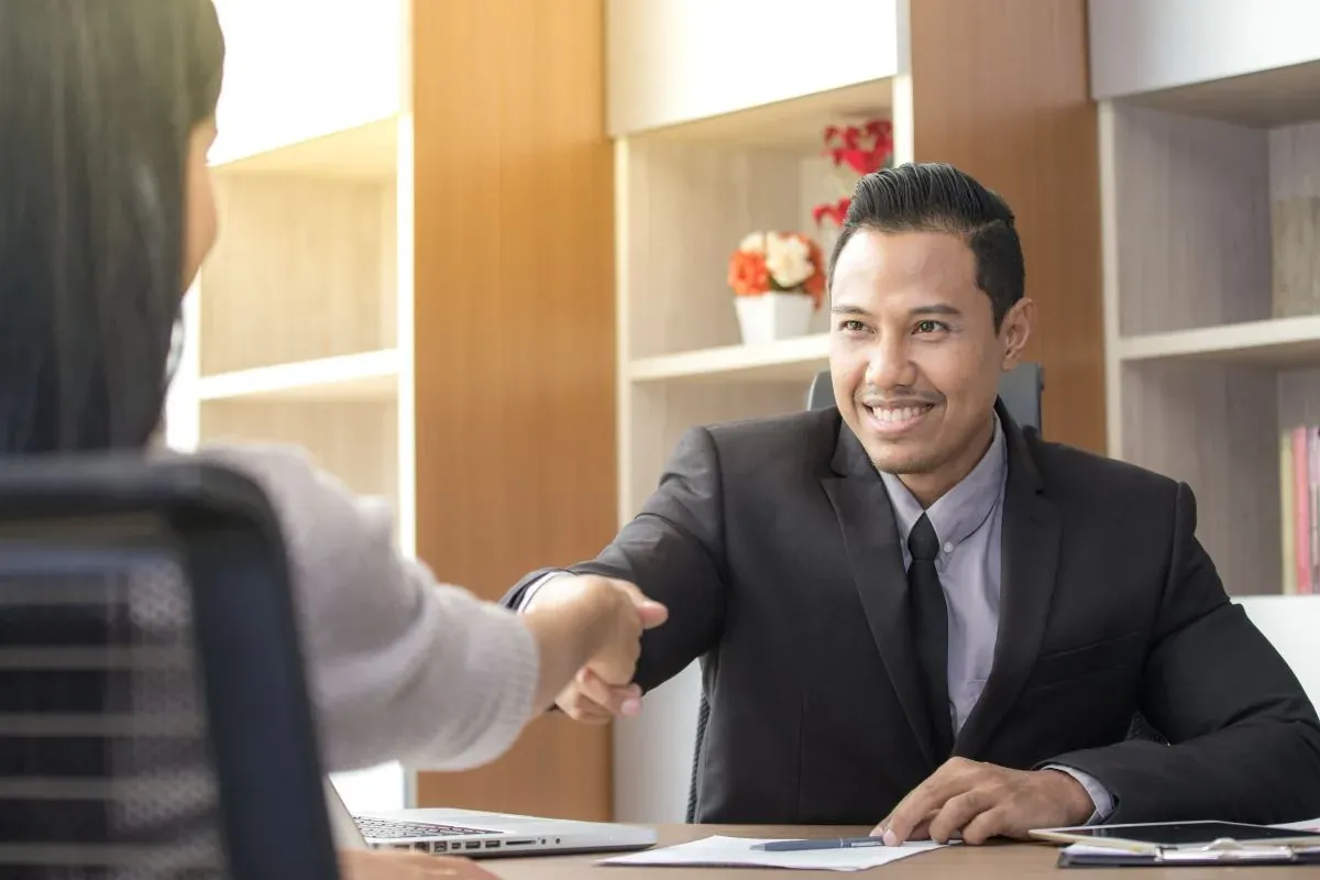 Smiling hiring manager shaking hands with a candidate across a desk during an interview