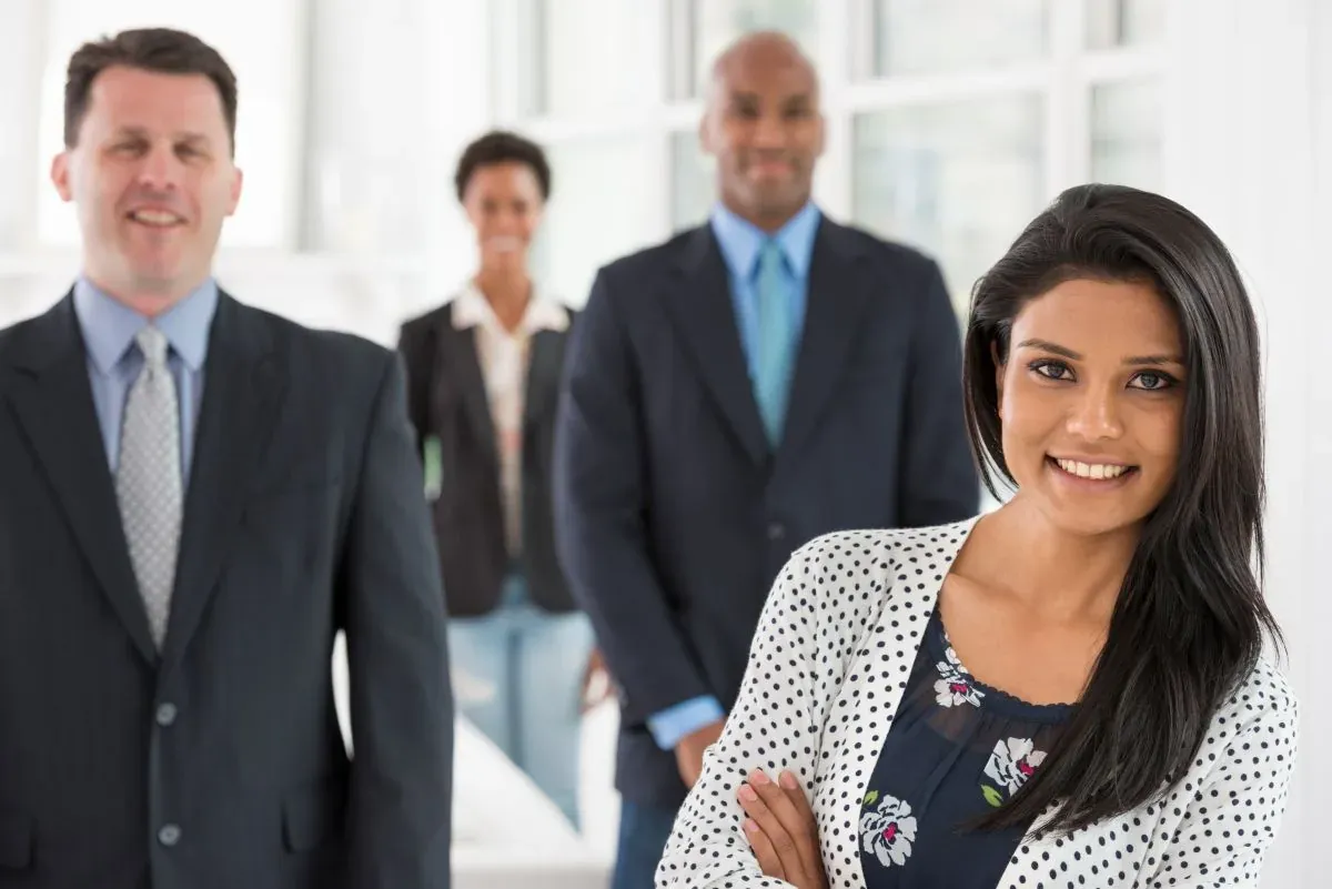 Smiling professional woman with arms crossed in front of three colleagues in a bright office